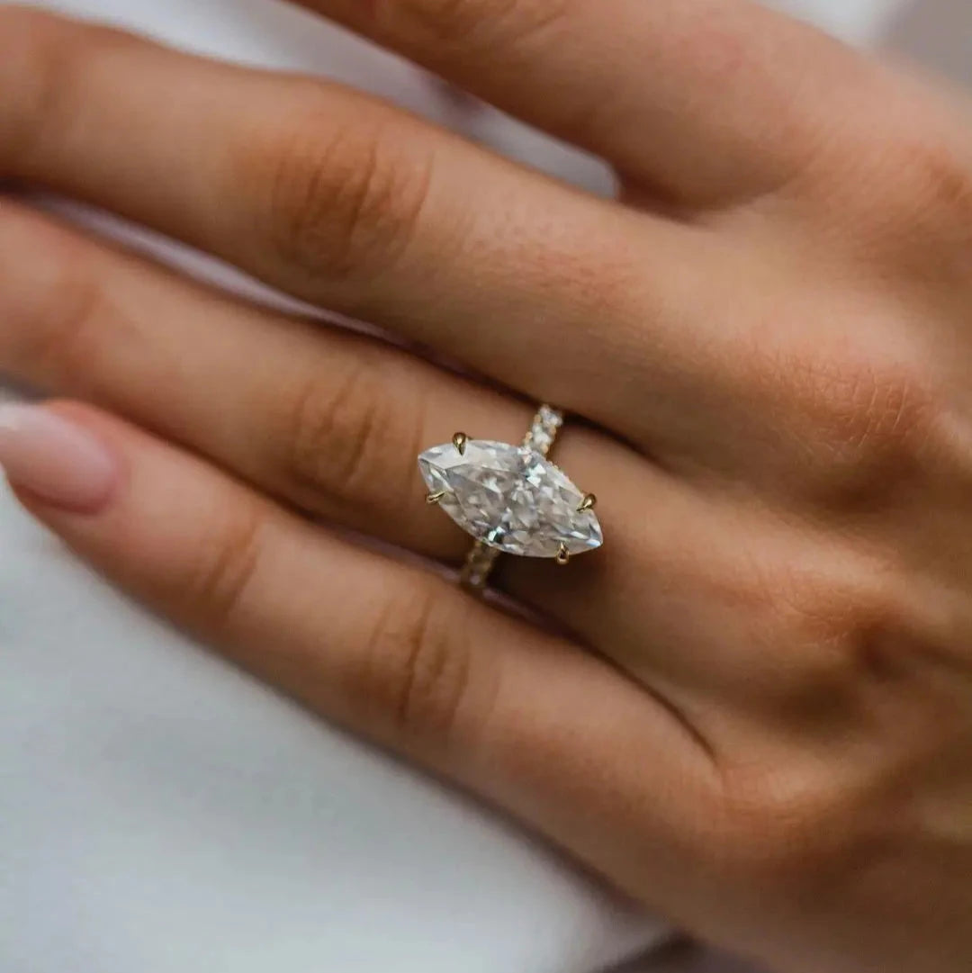 A hand wearing a silver engagement ring with a marquise cut central stone, surrounded by smaller round stones, set on a white background.