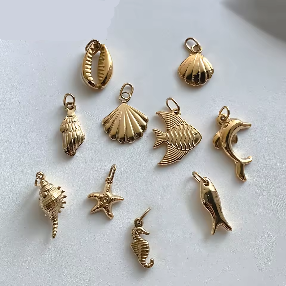 Gold stainless steel jewelry charms on a light gray background with 'Manco' branding.