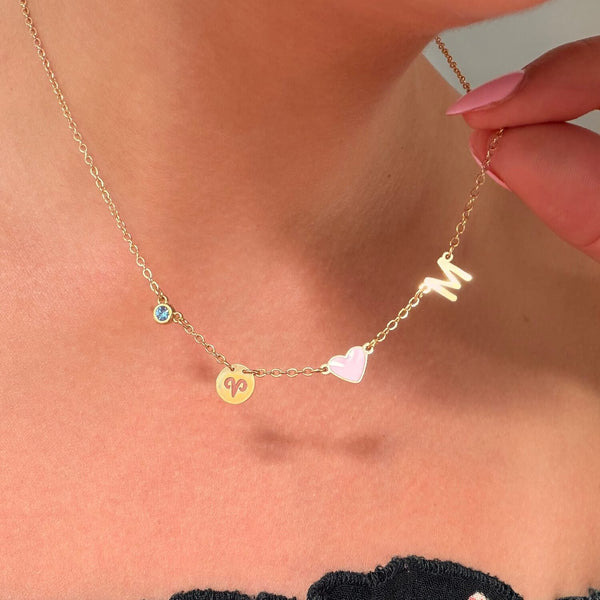 Gold necklace with heart and letter 'M' pendant on a person's neck and Virgo zodiac coin