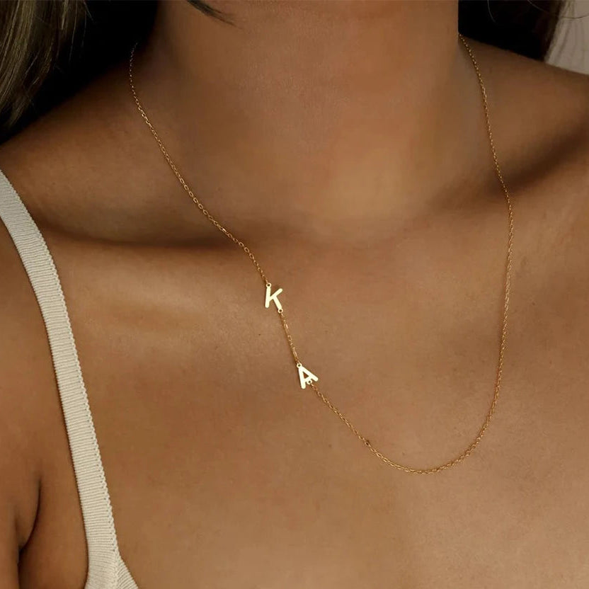 Gold necklace with 'K' and 'A' charms on a person wearing a beige top.