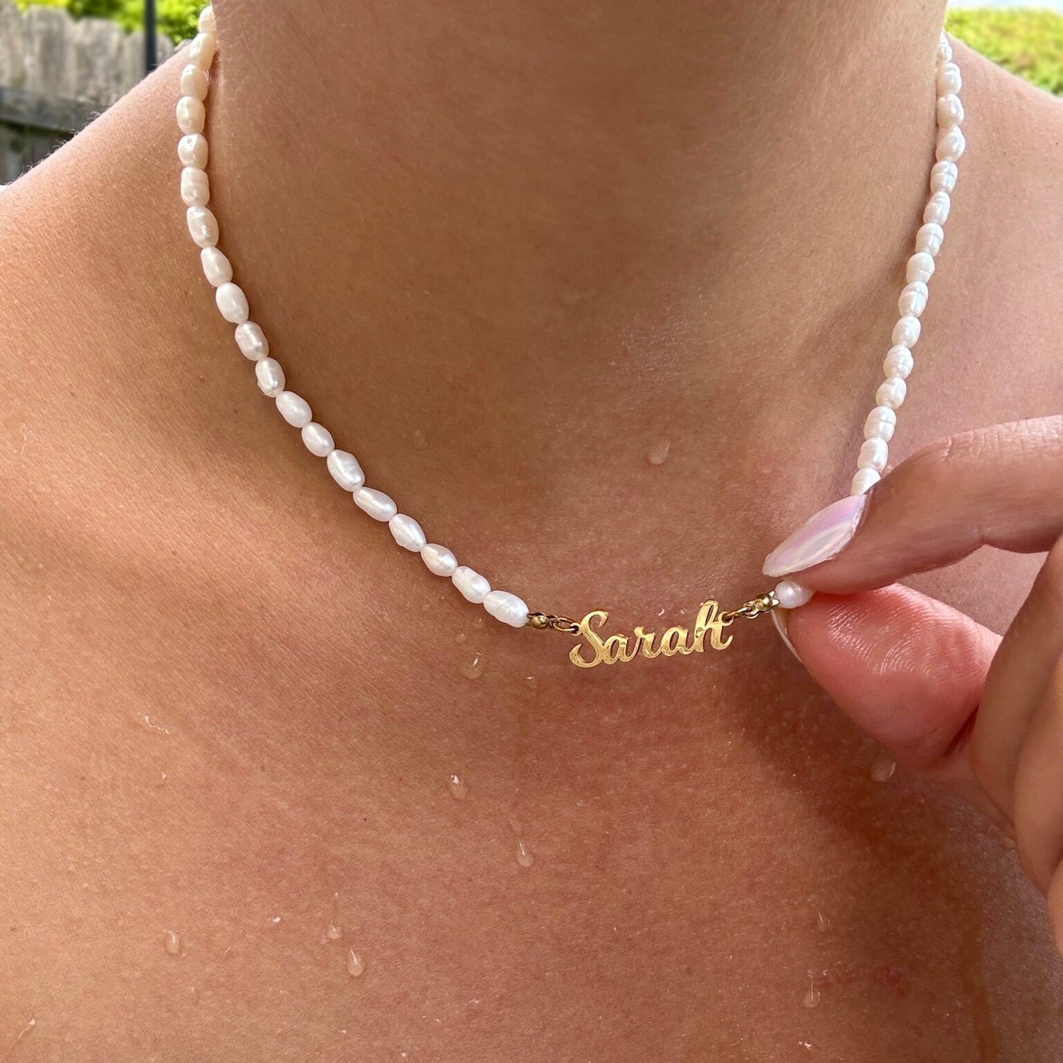 Pearl necklace with a gold nameplate 'Sarah' on a person's neck.